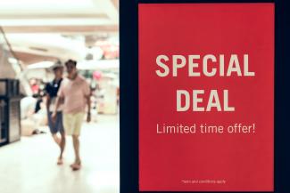 adults walking by a sign advertising a special deal